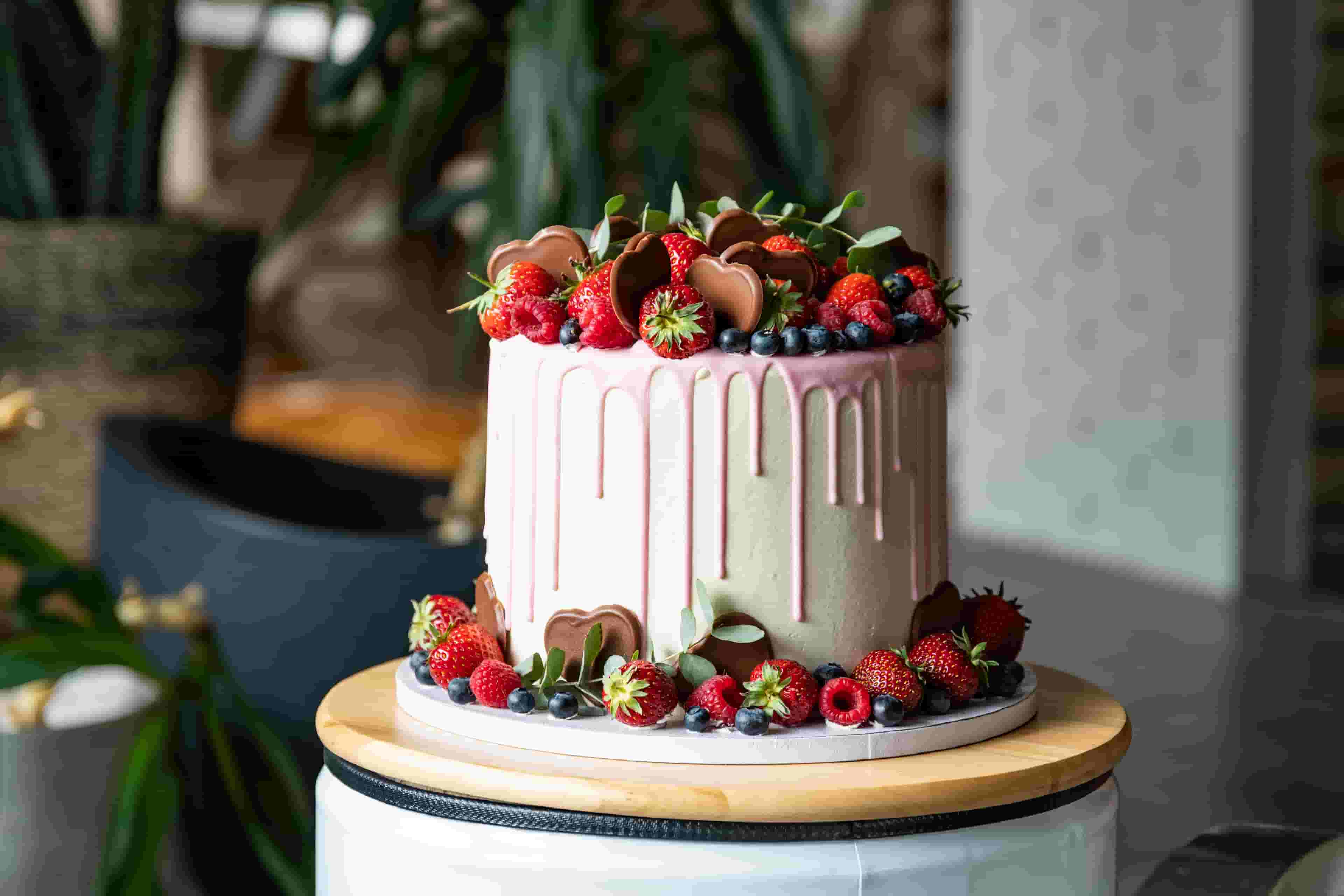 White Birthday Cake with Pink Drip, Strawberries and Chocolate on top.
